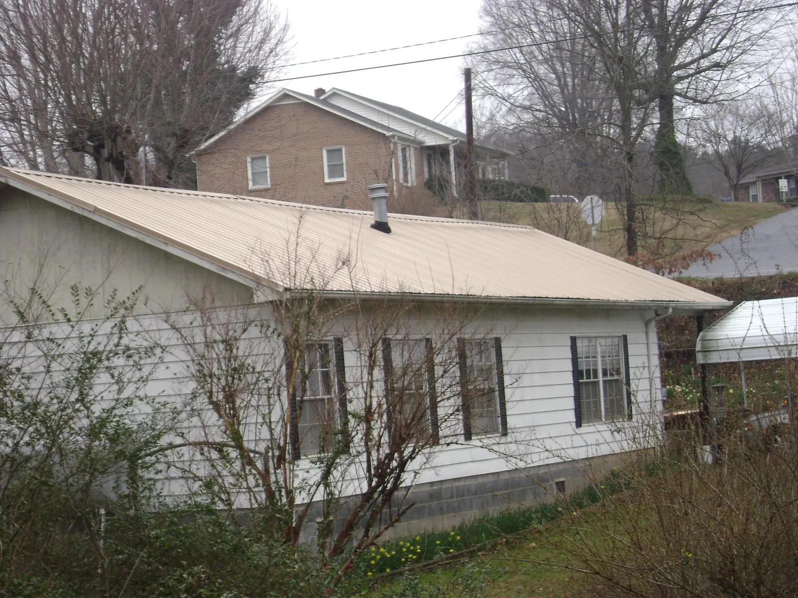 Tan metal roof on a white sided house set into a hillside — Commercial Roofing by Roofing Brothers in Perryville